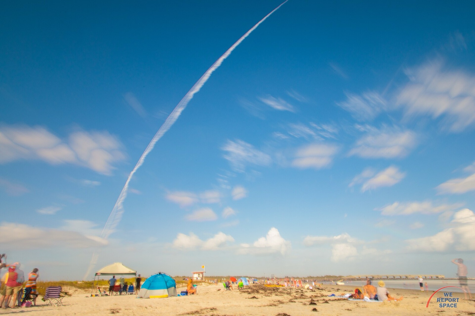 People on Jetty Park beach watching an Atlas V rocket climb into the sky