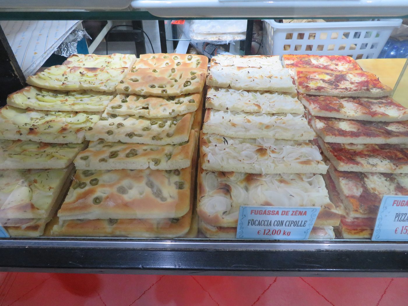 Trays of focaccia with olives, onion and potato in a Genoa bakery case