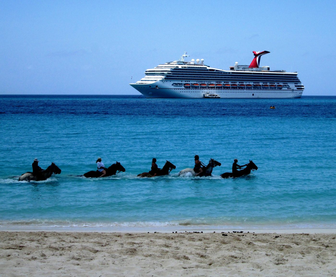 Tourists on horseback in the water at Half Moon Cay with a Carnival ship behind