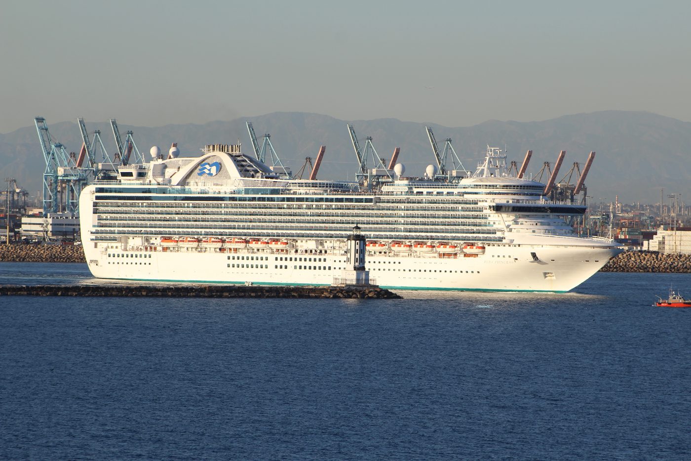 A cruise ship leaving the Port of Los Angeles with cranes behind